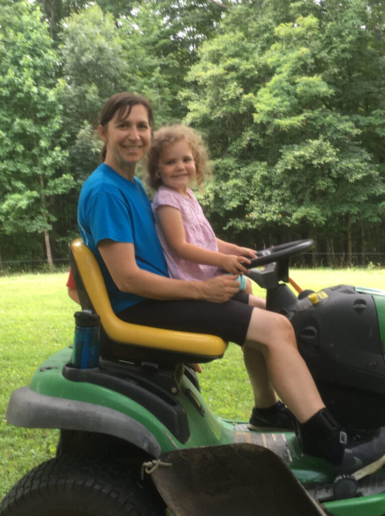 mother and daughter riding on a lawn mower. Mother mowing with a child on her lap.