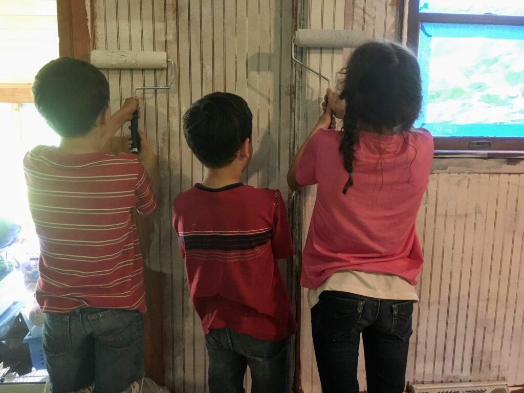 Three little kids put primer on wood paneling living room walls.