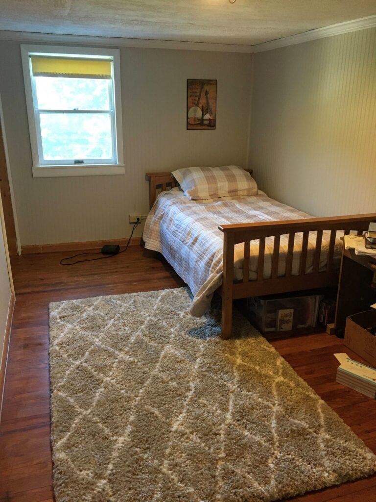 beige painted wood paneled bedroom with buffalo checked quilt and Moroccan rug