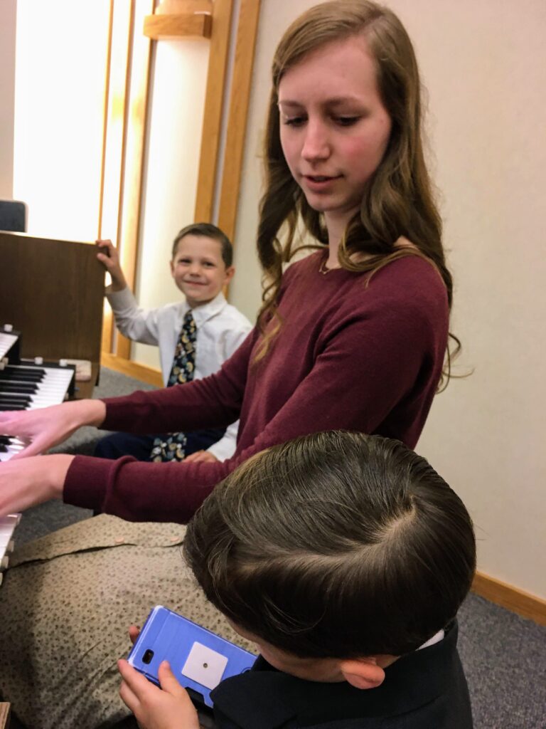 Teenage girl playing the organ at church with 2 little brothers by her side.