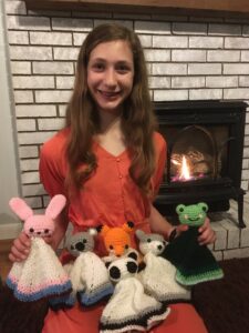 12 year-old holding 6 crocheted animal loveys she made. Bunny, koala, fox, panda, wolf, and frog.