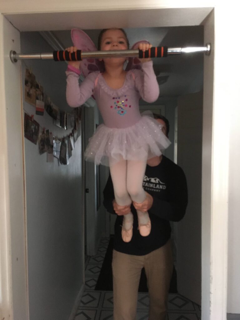 5 year old girl in purple ballet outfit doing a chin up on a chin up bar