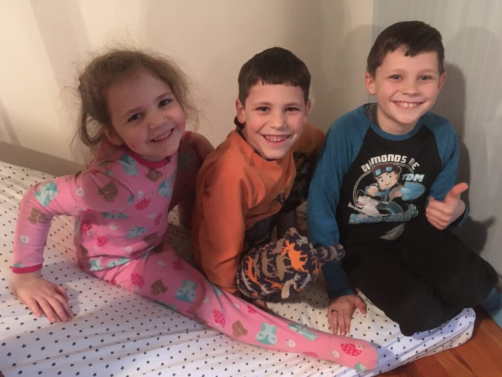 three kids at the bottom of the stairs after sliding down on a mattress