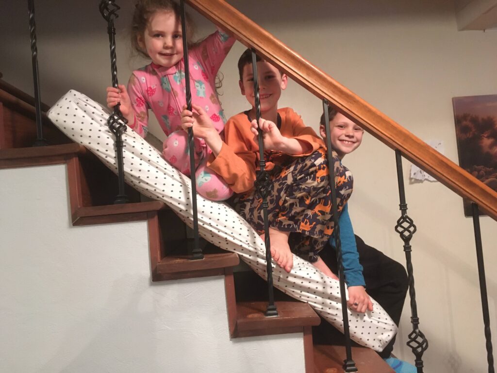 Three kids sliding down the stairs on a mattress.