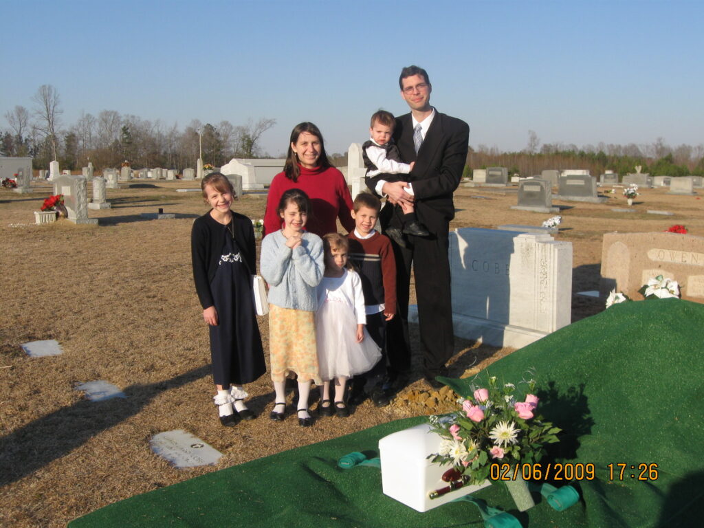 young family with 5 little kids standing by the grave of their stillborn baby
