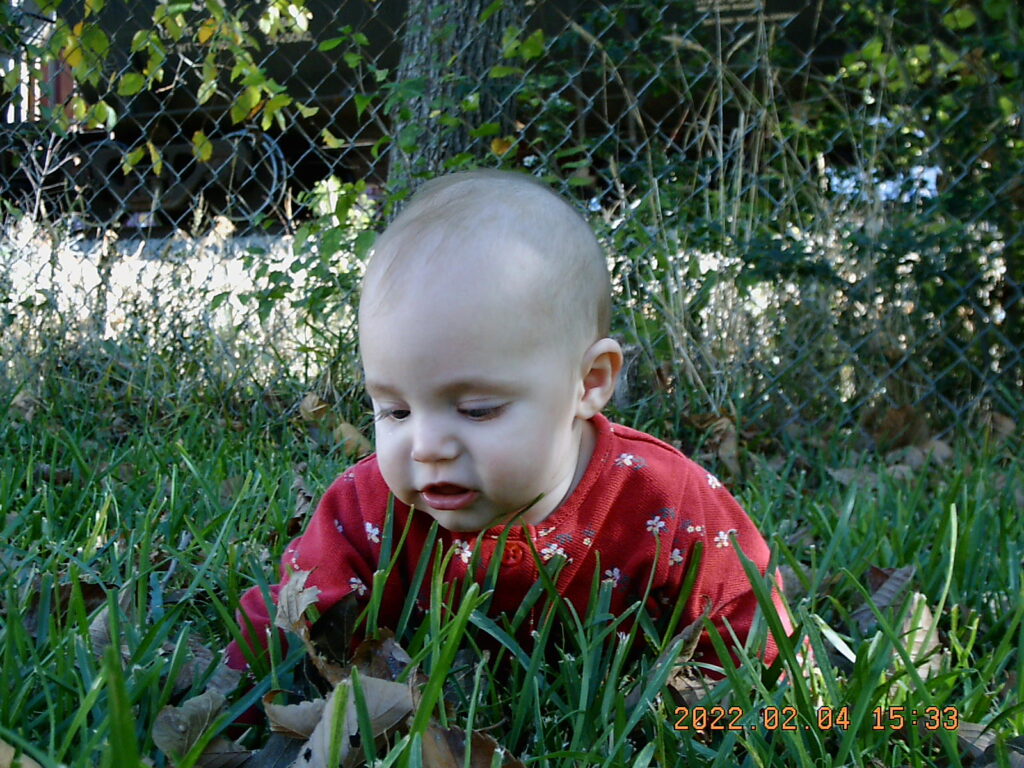A baby wearing red lying in the grass.
