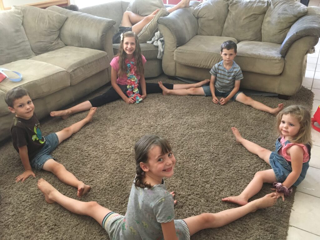 5 kids practicing their splits for fun on the living room floor.