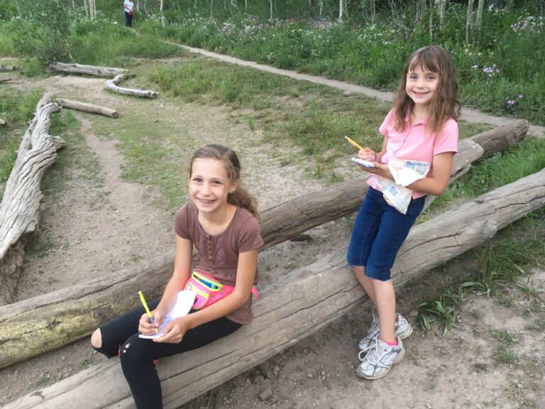 two girls drawing in sketch books out at nature school