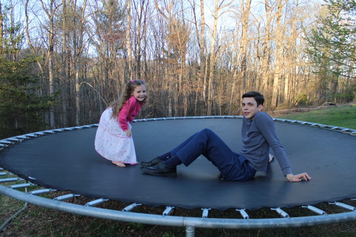 Little girl and brother hanging out on the trampoline.