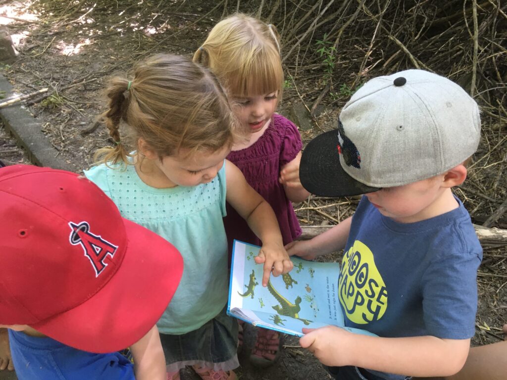 4 little kids looking at a book at nature school