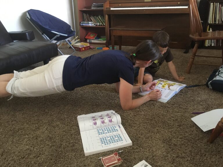 mom doing a plank while helping child with schoolwork.