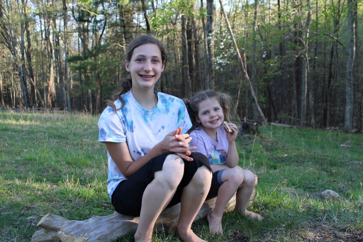 two sisters sit on a log eating their s'mores.