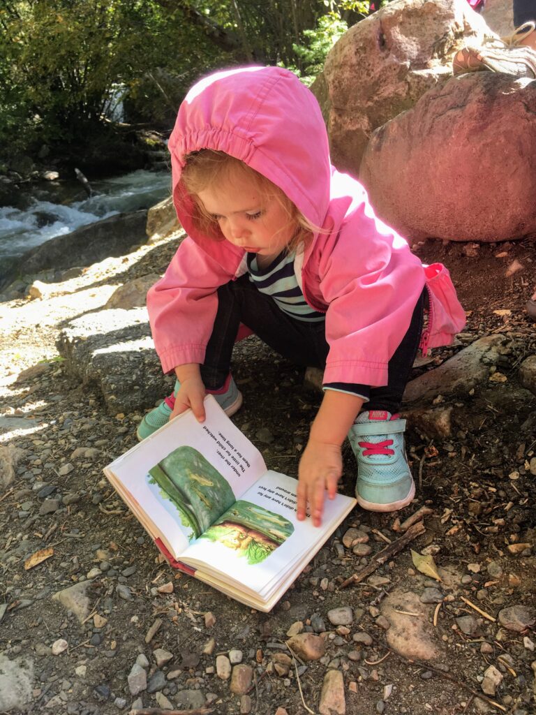 toddler girl reads a book outside