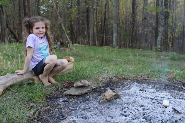 5 year old girl props her stick up with a rock to roast her marshmallow