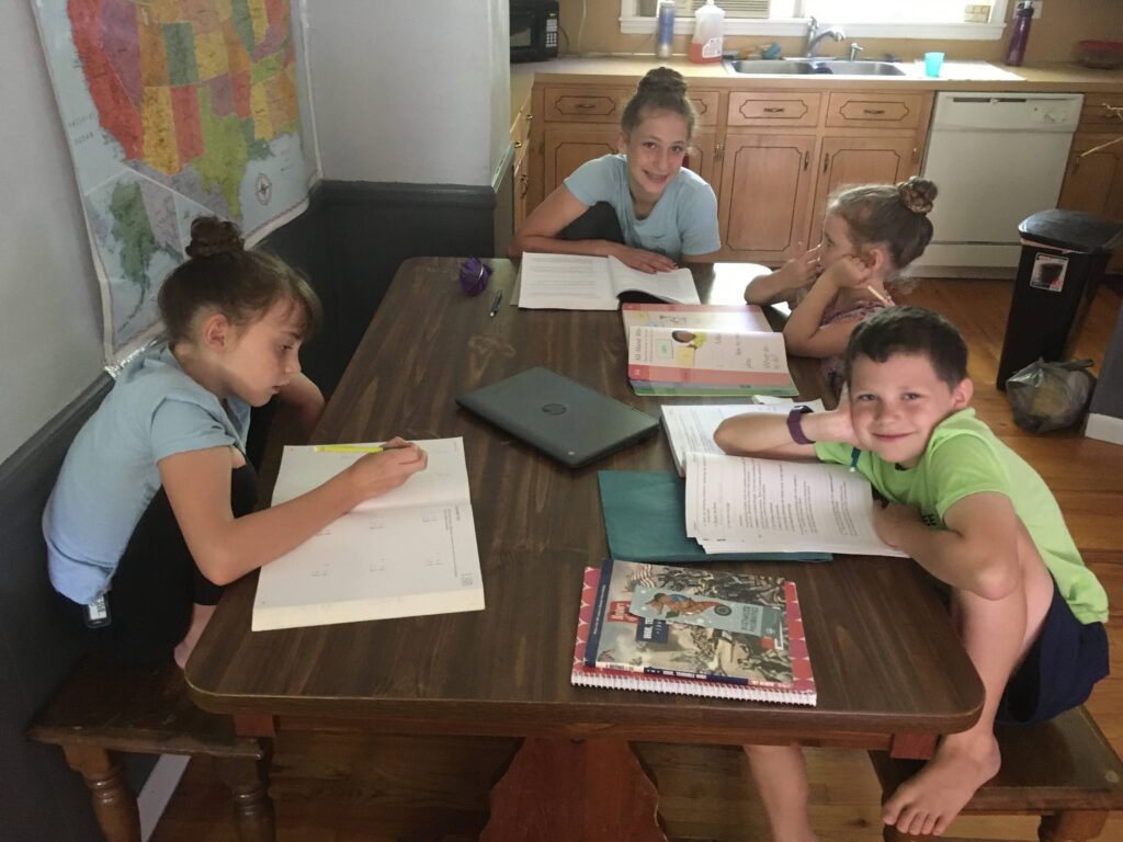 4 kids doing their school around the dining room table in their homeschool classroom.