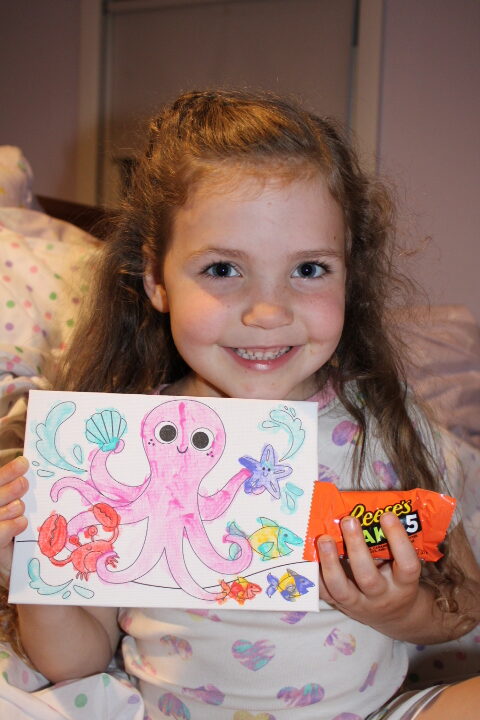 girl shows the camera her painting and a candy bar she left on her moms pillow for a surprise.