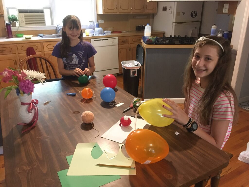 two girls make a solar system out of balloons in their homeschool