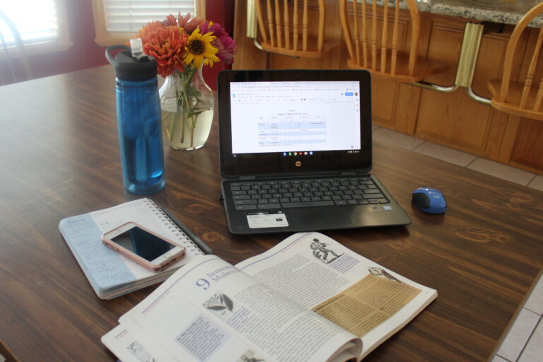 a chromebook, US history textbook, planner and water bottle to do lesson planning for homeschooling