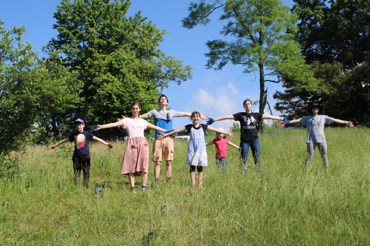 Mom and 6 kids standing in a field with their arms out and smiling