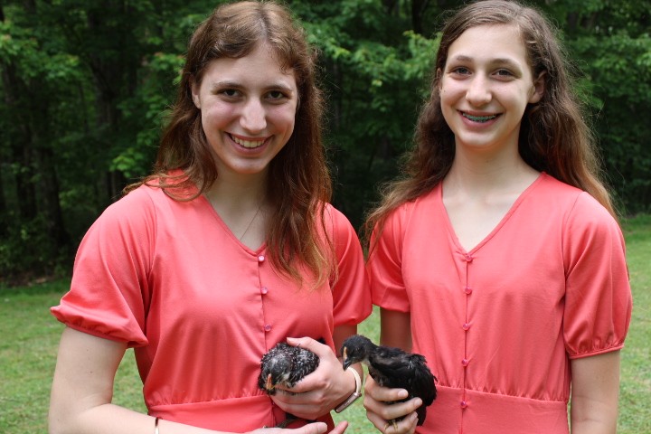 two sisters with matching dresses hold chicks.