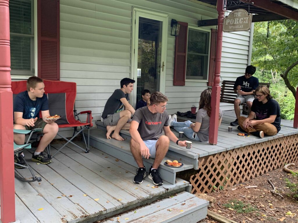 teens eating pizza on the front porch of a country house