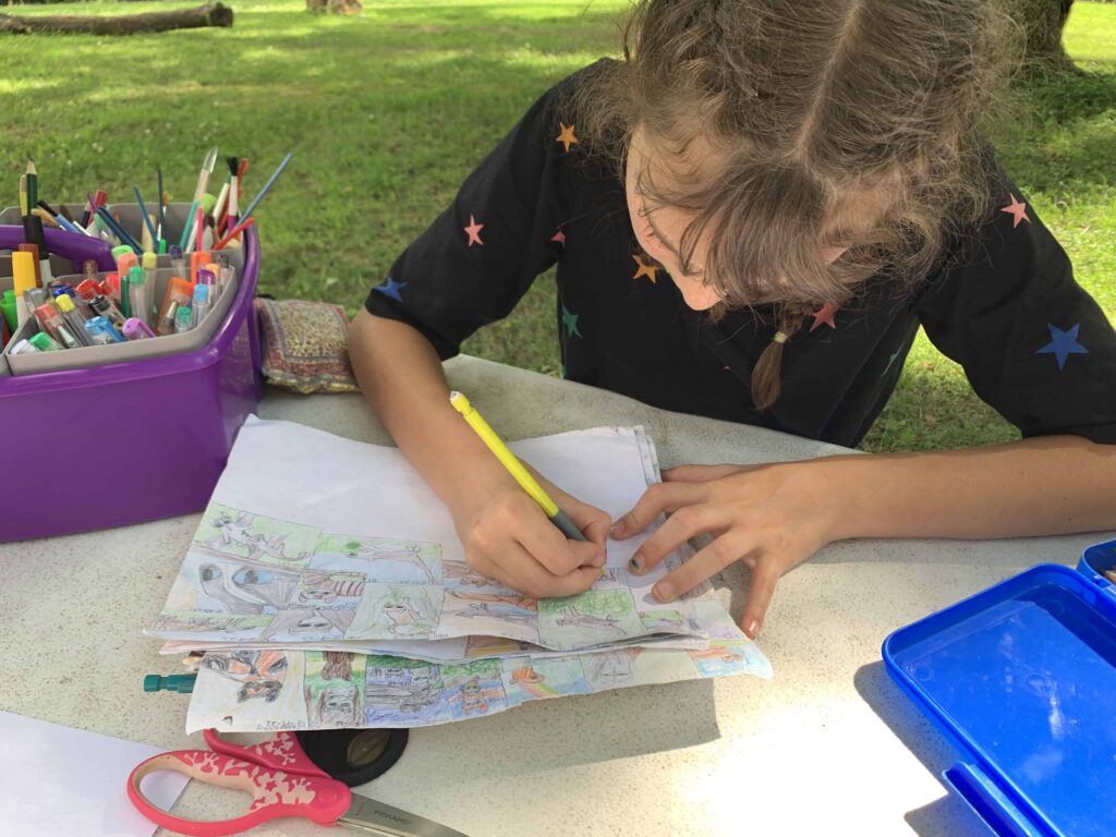 a girl draws on a piece of paper at the picnic table