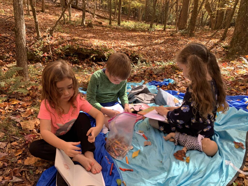 3 little kids sitting on a blanket in the woods, drawing