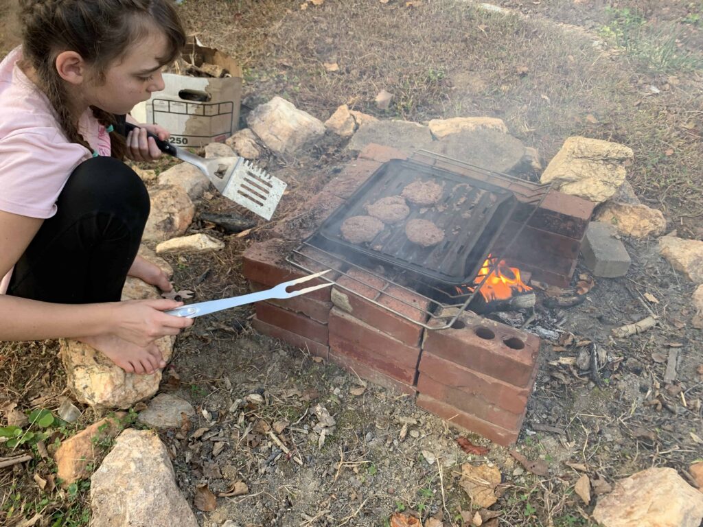 girl cooking hamburgers over campfire