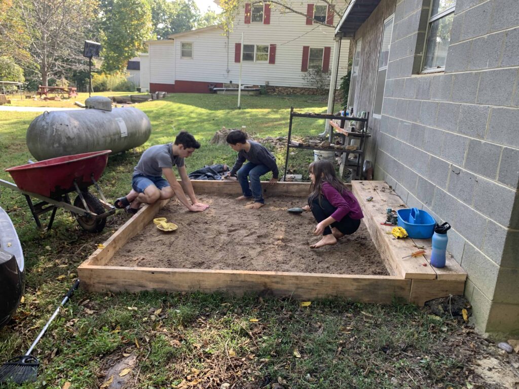siblings unloading sand into a sandbox