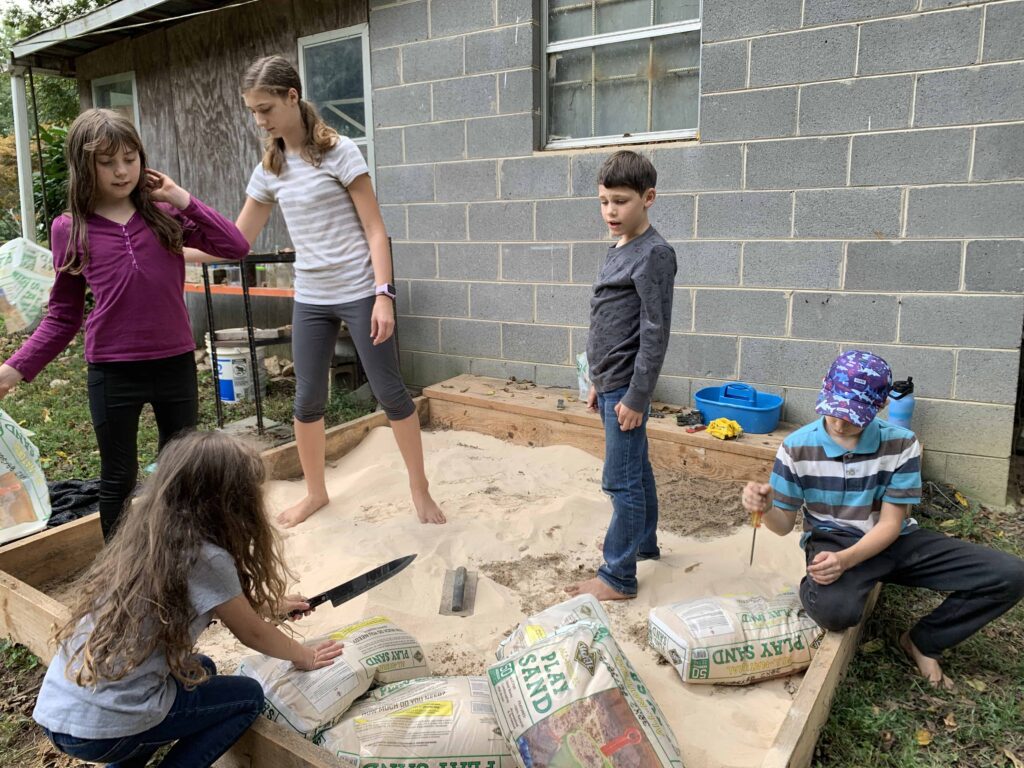 siblings unloading sand into a sandbox