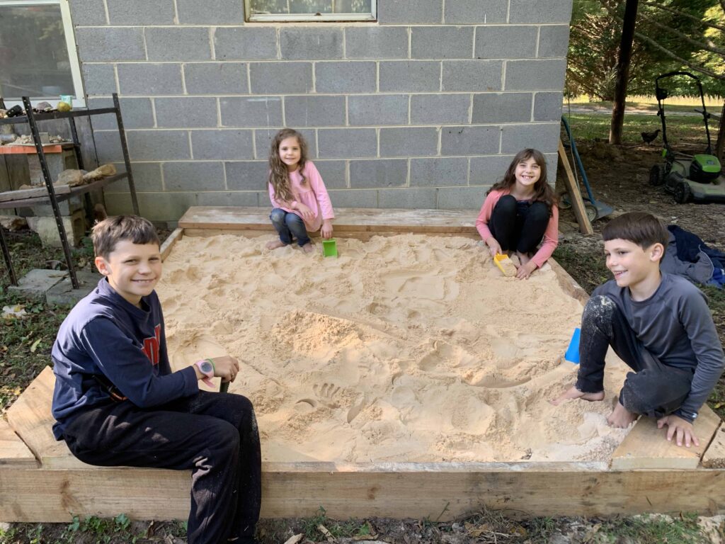 sandbox with new sand and 4 kids playing in it