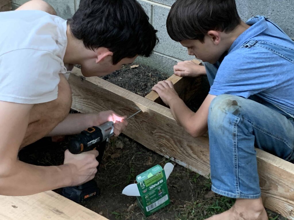two brothers screw in parts of a sandbox they're building out of wood